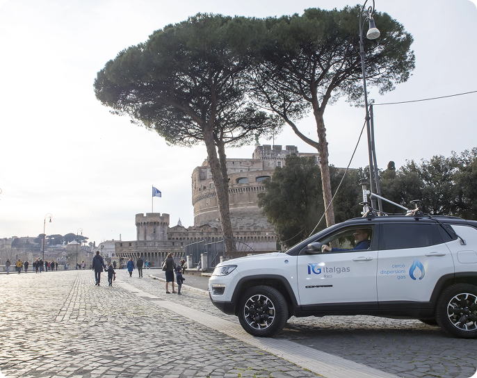 A white Italgas SUV is parked on a cobblestone street near a historic castle in Rome. Tall trees border the scene, creating a serene atmosphere.